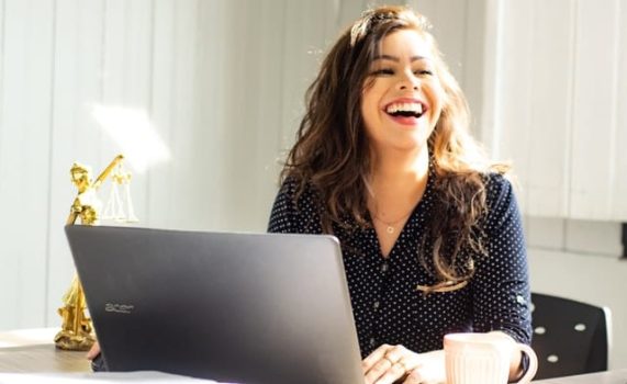 Une jeune femme face à son ordinateur se réjouit de la notoriété de son site